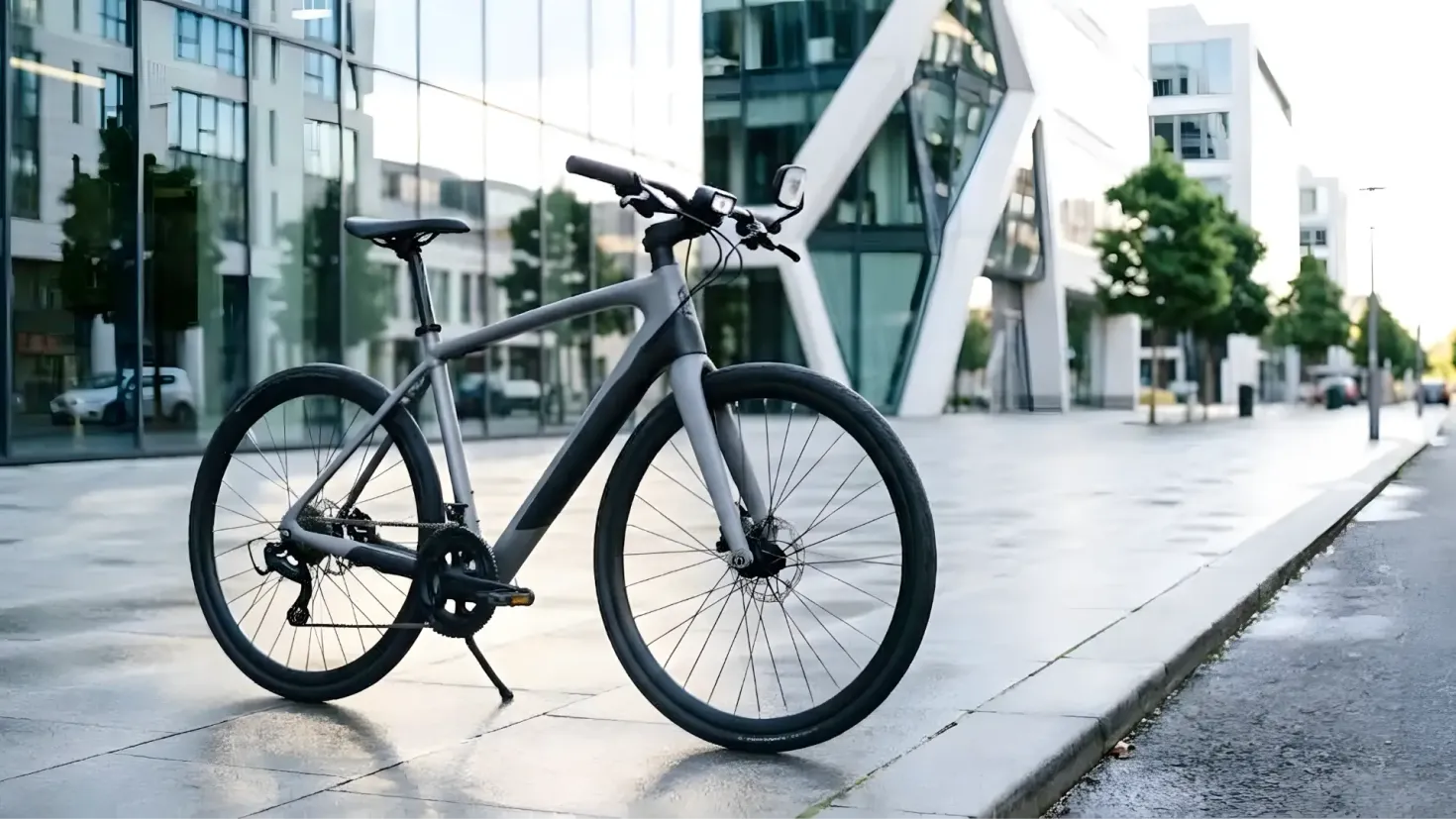A modern grey bike parked on a city sidewalk in front of a contemporary glass and concrete office building.