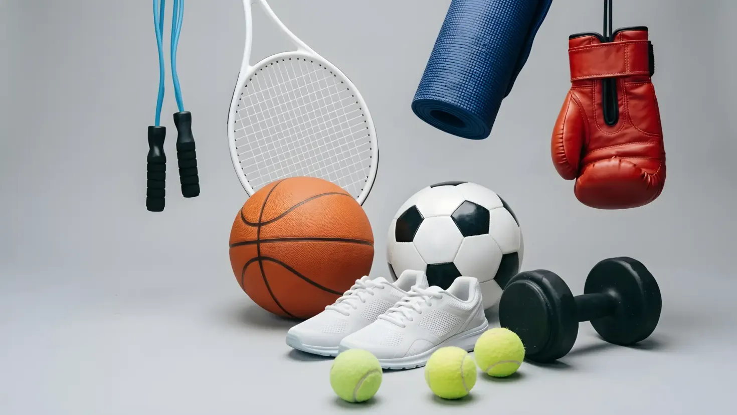 Multi-sport equipment collection on a grey background, featuring a tennis racket, basketball, soccer ball, boxing glove, dumbbell, and sneakers.