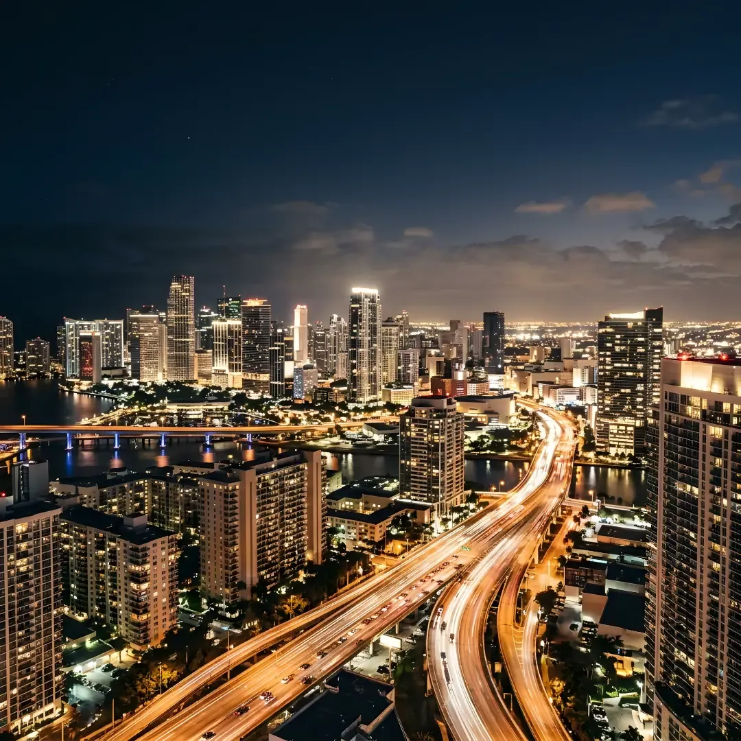 A high-angle long exposure photo of a sprawling city skyline at late evening, featuring illuminated skyscrapers and glowing traffic light trails along highways without any visible people.